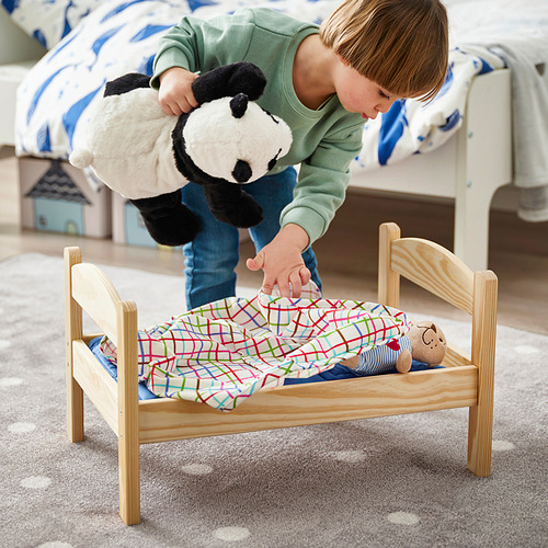 Un niño mete un gran panda de peluche en una cama de juguete de madera con una manta de colores, promoviendo el juego de simulación.