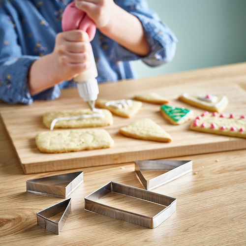 Una persona decora las galletas con glaseado en una tabla de madera, utilizando varios cortadores de galletas.