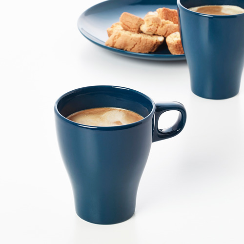 Dos tazas azules llenas de café, colocadas sobre una mesa blanca, acompañadas de un plato con galletas.