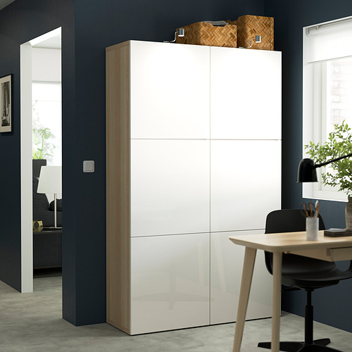 Mueble de almacenamiento BESTÅ blanco contra la pared azul oscuro, alto con múltiples compartimentos, diseño moderno y elegante.