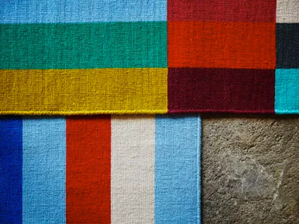 Woven rug samples featuring vibrant color blocks and stripes on a concrete floor.