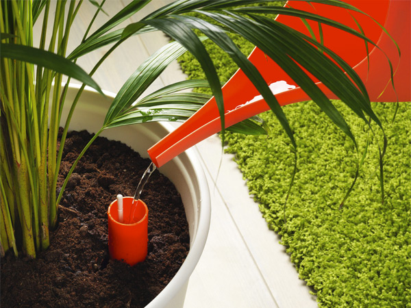 Orange watering can pouring water into a self-watering pot insert.