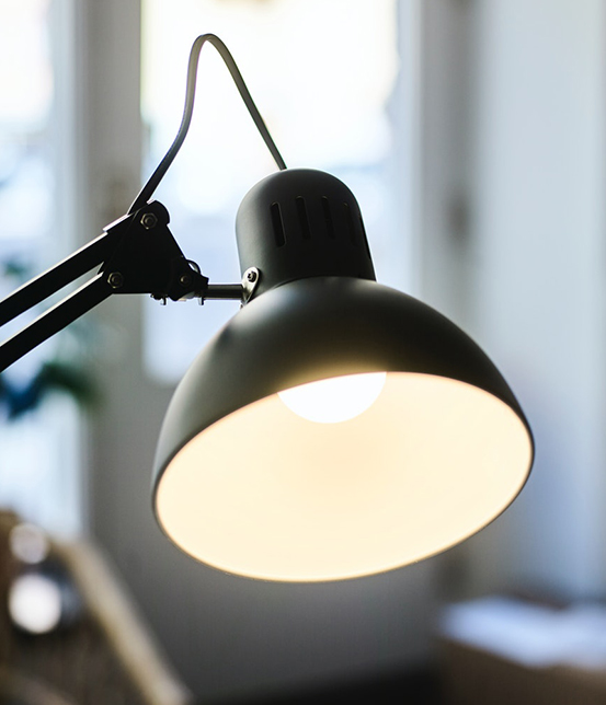 Close-up of a black desk lamp with a warm light and adjustable arm, in a bright indoor setting.