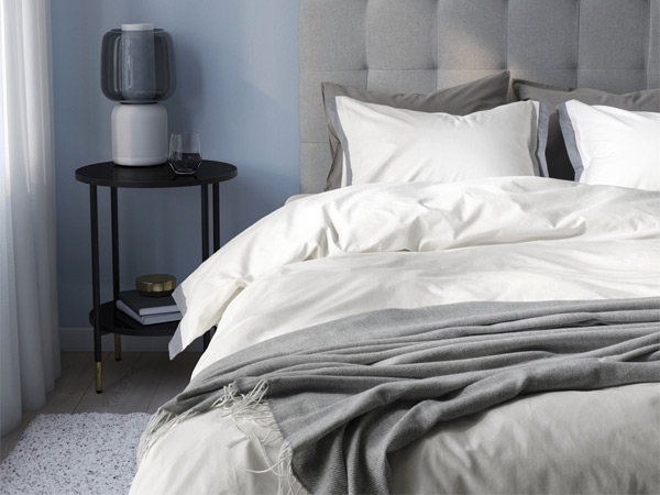 Bed made with white bedding, gray throw blanket, and a bedside table with lamp.