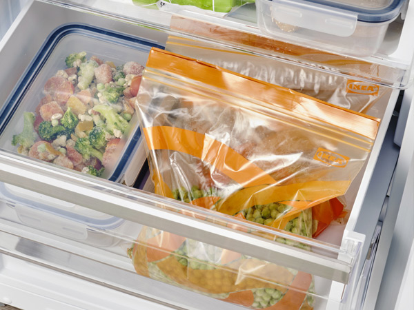 Reusable zip-top bags with frozen vegetables inside a freezer drawer.