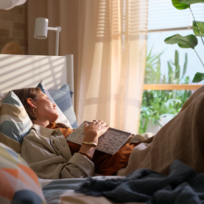 Woman sleeping peacefully in bed holding a book on her chest.