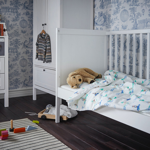Un cuarto de bebé con una cuna SUNDVIK a la derecha con un peluche GOSIG GOLDEN encima y un armario SUNDVIK.
