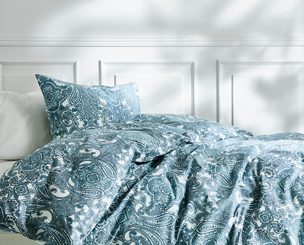  A bed with a blue and white paisley duvet cover and a white pillow.
