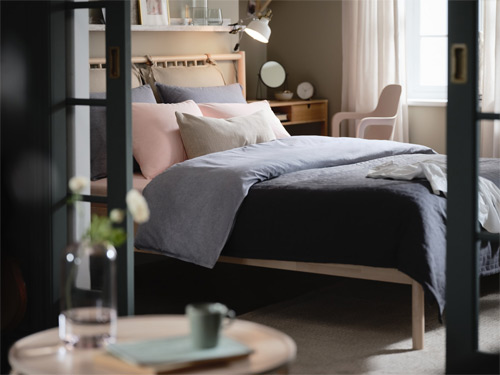 Cama acogedora con edredón azul y cojines rosados vista a través de una puerta corredera.
