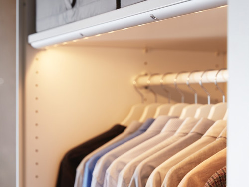 Tira de luz LED integrada iluminando Camisas colgadas dentro de un armario blanco.