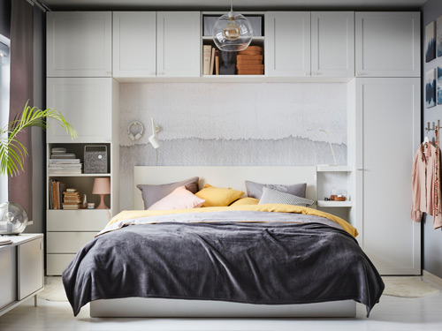 Dormitorio moderno con cama doble rodeada por un sistema de armarios blancos modulares.