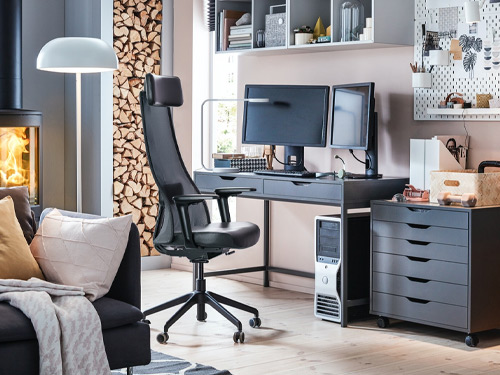 Zona de trabajo en casa con escritorio gris, dos monitores y silla ergonómica negra.