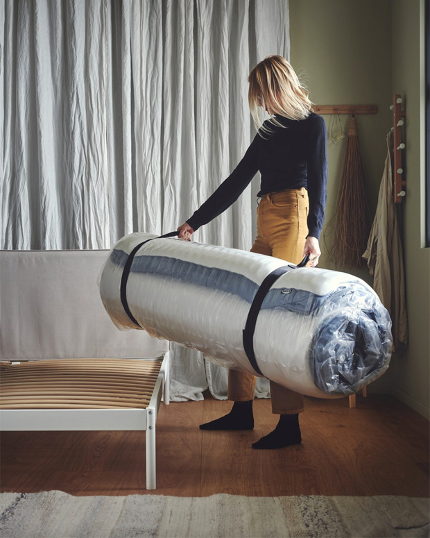 Mujer sujetando un fardo con un colchón enrollado listo para colocar en la cama