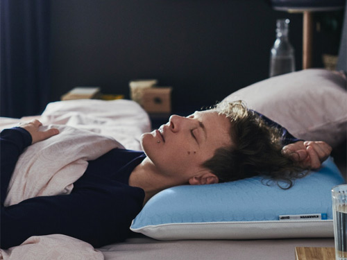 Persona durmiendo placenteramente en una cama sobre una almohada ergonómica azul.