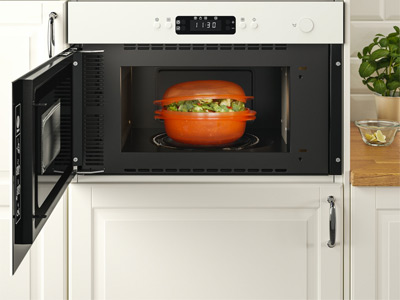 Horno microondas empotrado abierto con un recipiente naranja con verduras dentro.