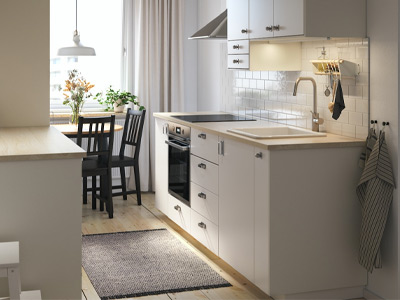 Cocina blanca moderna con encimera de madera, electrodomésticos y mesa de comedor al fondo.