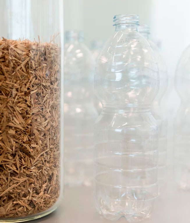 Botella de vidrio con virutas de madera a la izquierda; varias botellas de plástico vacías y transparentes a la derecha.