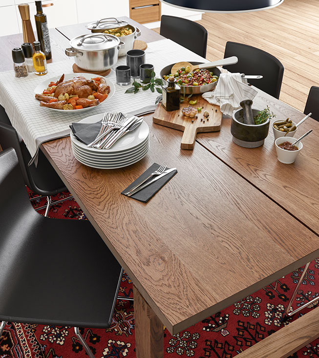Una mesa de comedor de madera lista con comida, platos y cubiertos, sobre un tapete rojo.