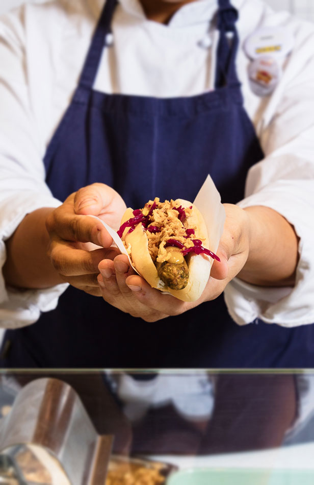 Chef sosteniendo un hot dog veggie frente a la cámara, destacando una opción deliciosa y sostenible sin carne.