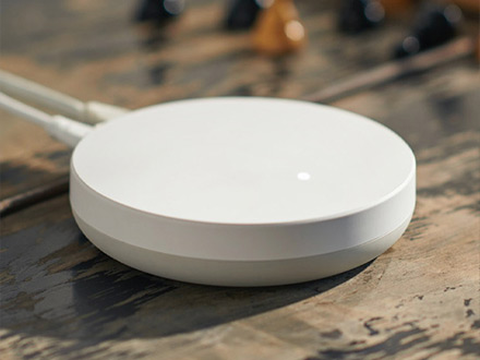 Hub inteligente blanco circular con luz led indicadora sobre una mesa de madera.