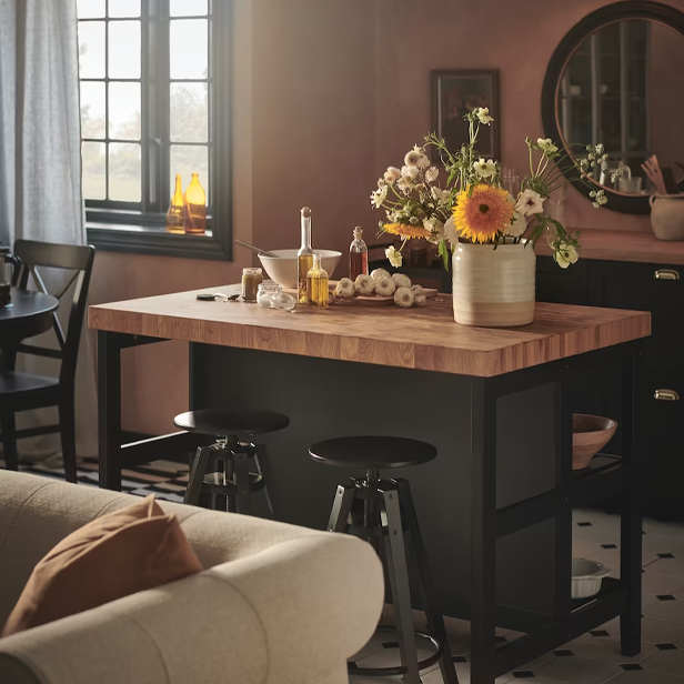 Una isla de cocina con superficie de madera y base negra, con flores y utensilios, en un ambiente cálido.