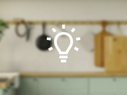 Dibujo vectorial en blanco de una bombilla iluminada con el fondo de una cocina tradicional completamente difuminado.