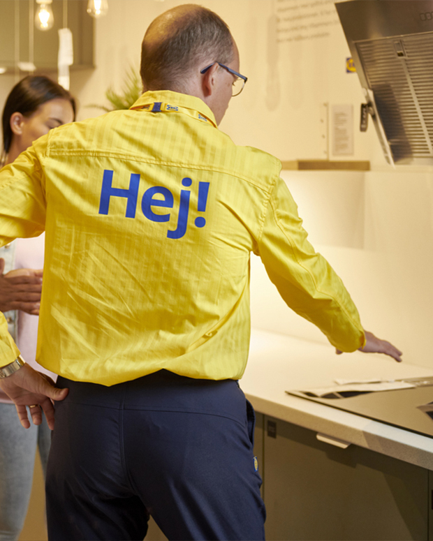 Persona del servicio de atención al cliente de IKEA, de espaldas, vestida con camisa amarilla a rayas con la palabra «hej» escrita en la parte posterior de la camisa.