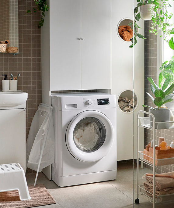 A laundry corner with a white washing machine, cabinets, and hanging plants, next to a sink. Clean and organized atmosphere.