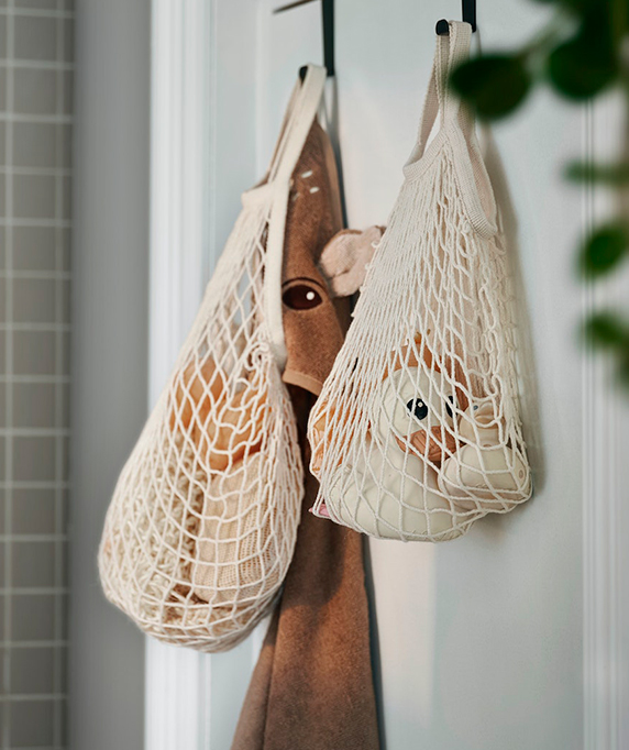 Two white mesh bags hang from hooks, holding plush toys and a brown towel. Child-friendly, tidy atmosphere.