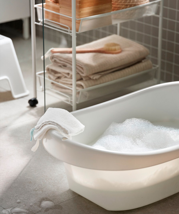 A white baby bathtub with bubbles, folded towels, and a shelf in a bathroom. Clean and functional atmosphere.