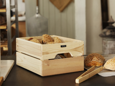 Una caja KNAGGLIG junto a unas pinzas para servir OSTBIT.