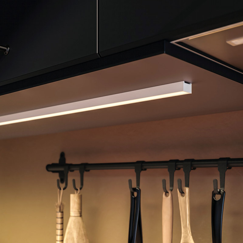 Iluminación LED bajo gabinetes negros de cocina, con utensilios colgando en una barra oscura debajo.