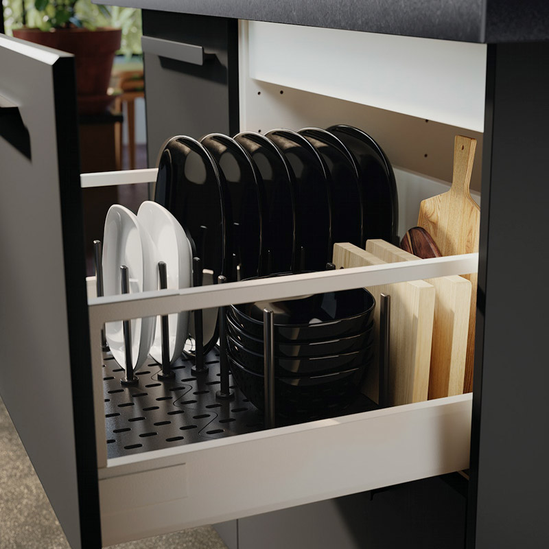 Cajón de cocina organizado con platos negros y blancos, cuencos y tablas de cortar de madera.