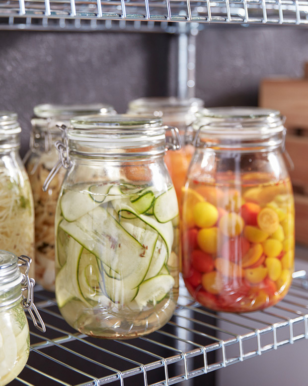 Various hermetic jars with colorful pickled vegetables on a metal shelf.