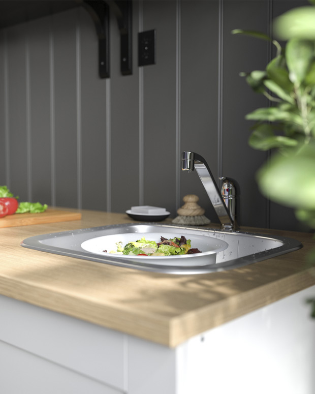Kitchen sink with plate of food, cutting board, and plant, featuring a modern faucet.