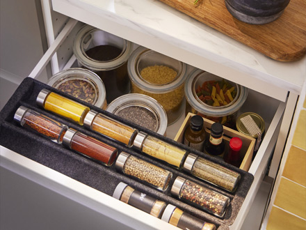 Cajón de cocina abierto con frascos de especias en un especiero y frascos de alimento.