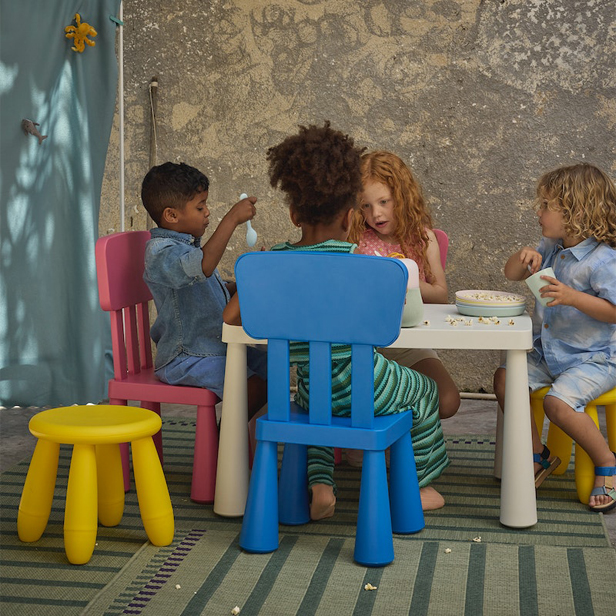 Vista posterior de niños sentados alrededor de una pequeña mesa blanca en sillas de color pastel