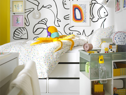Cama infantil con peluche de pulpo y pared decorada con dibujos marinos.