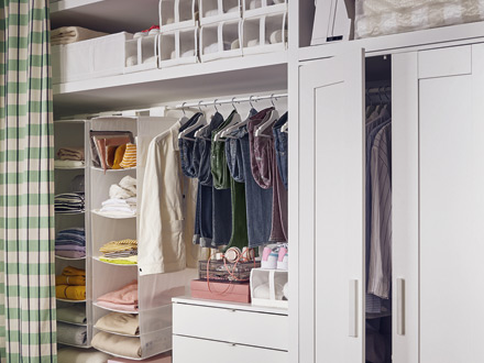 Vestidor blanco organizado con ropa colgada, estantes de tela y cajas.
