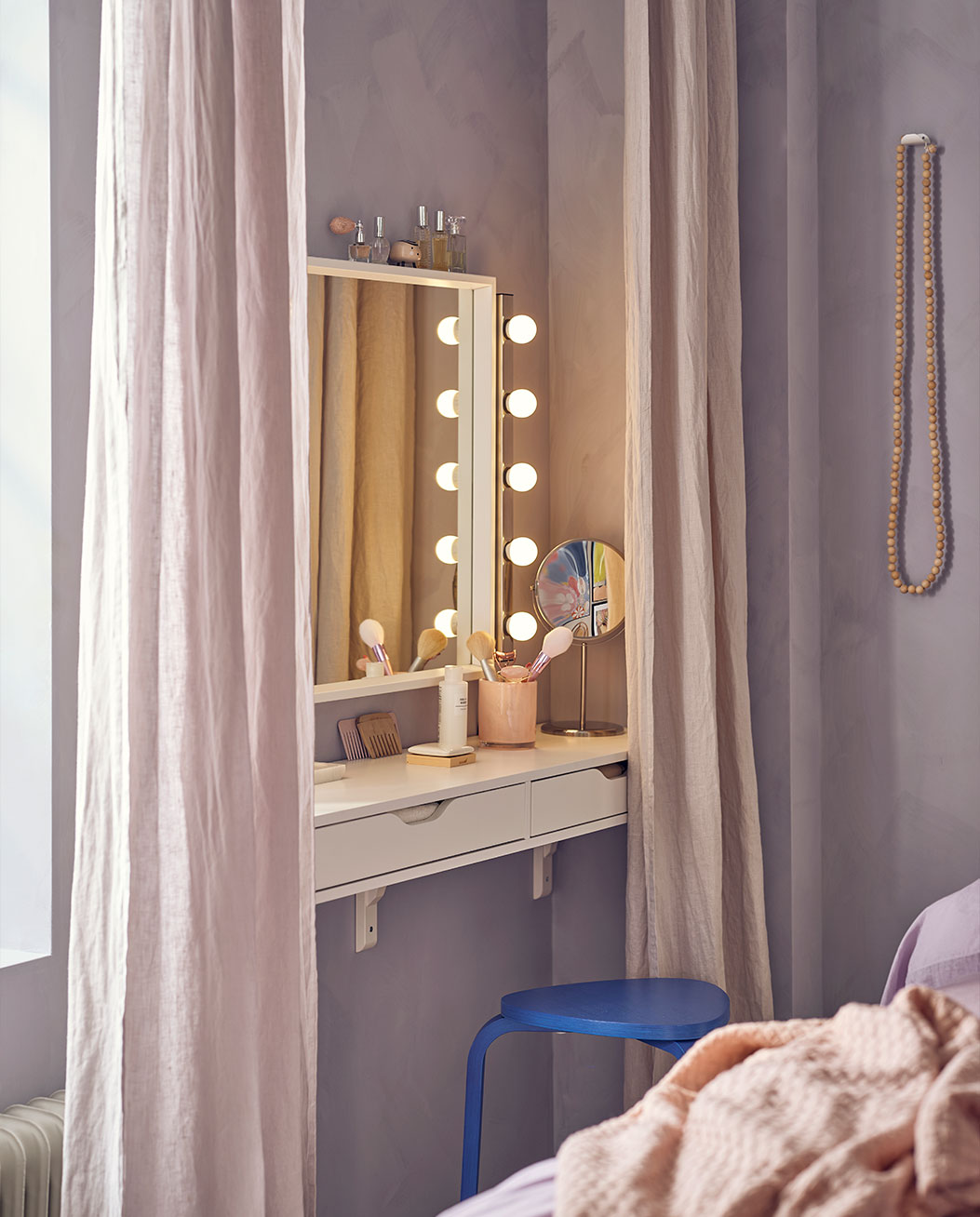 Espejo rodeado de luces junto a una consola de estanterías con cortinas suaves