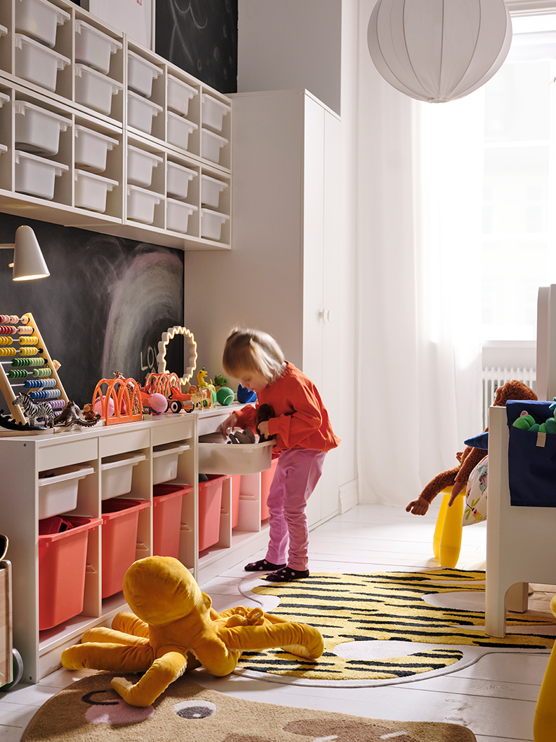 Una niña buscando juguetes dentro del sistema de almacenamiento TROFAST, y un pulpo de peluche BLÅVINGAD en el piso.