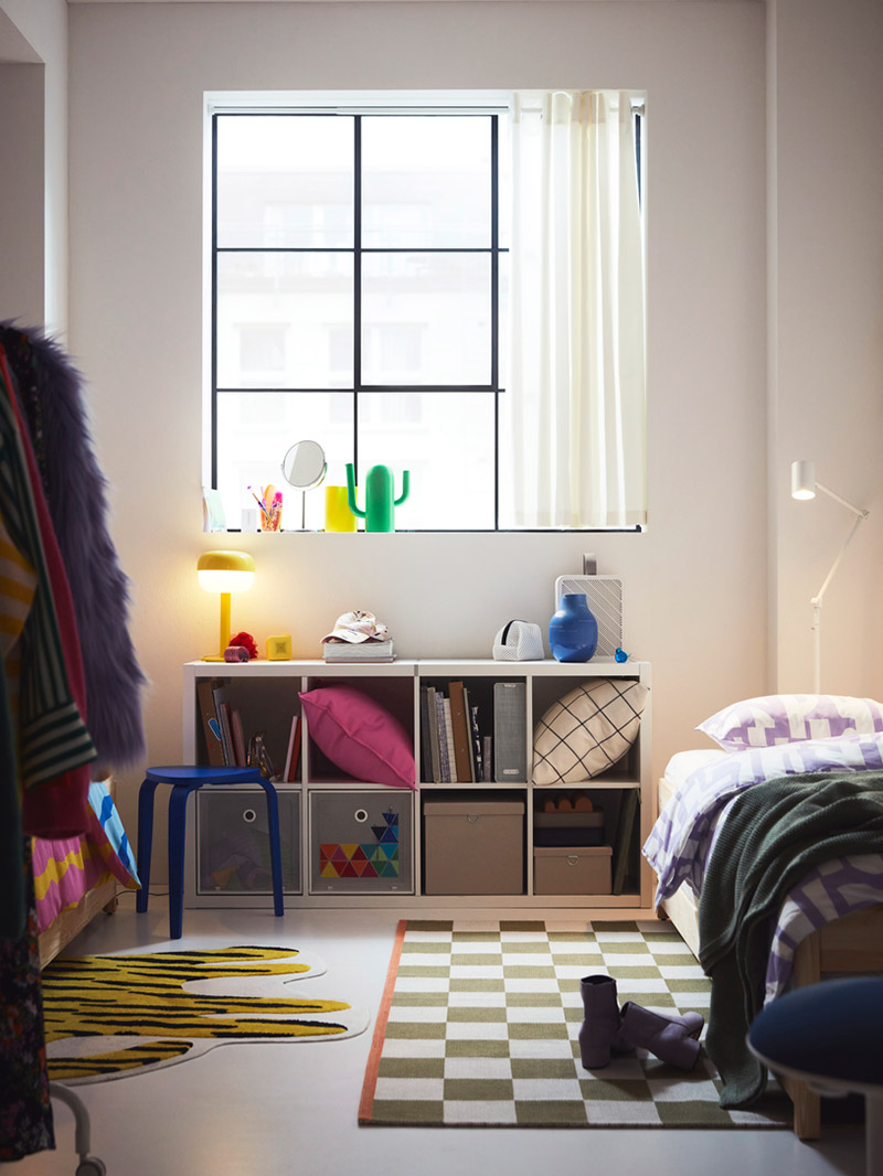 Bright youth bedroom with white shelves, colorful items, a checkered rug, and a single bed.