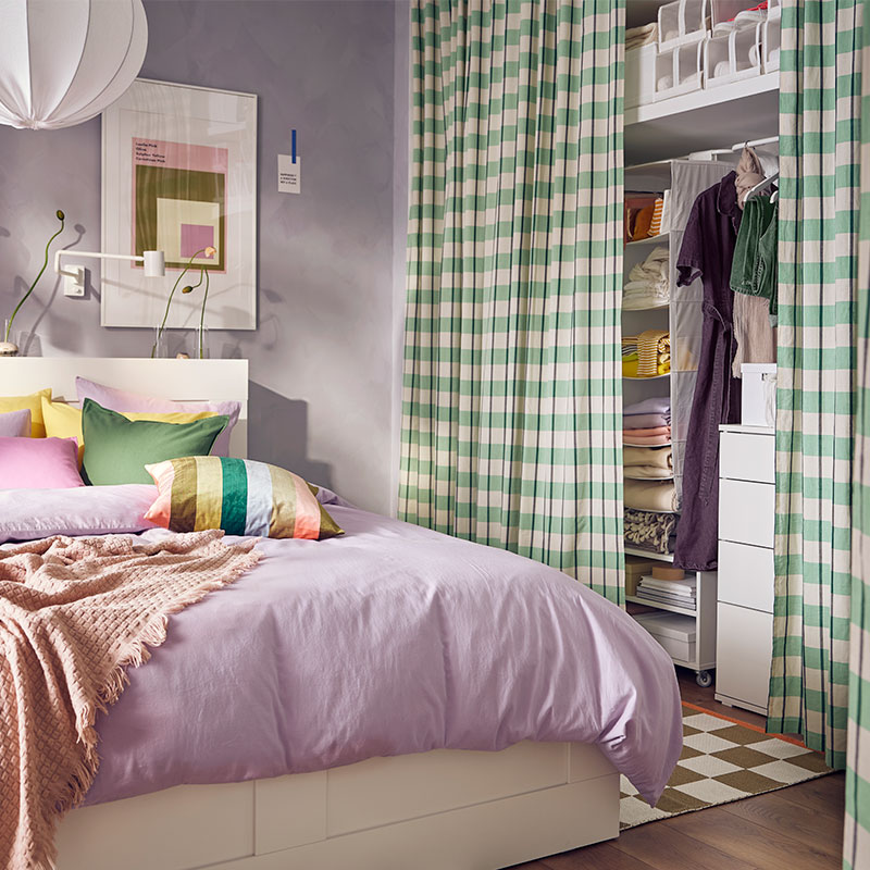Dormitorio colorido, una cama grande con cojines de colores vivos, una funda de color morado claro y un armario con cuadros escoceses de color verde.