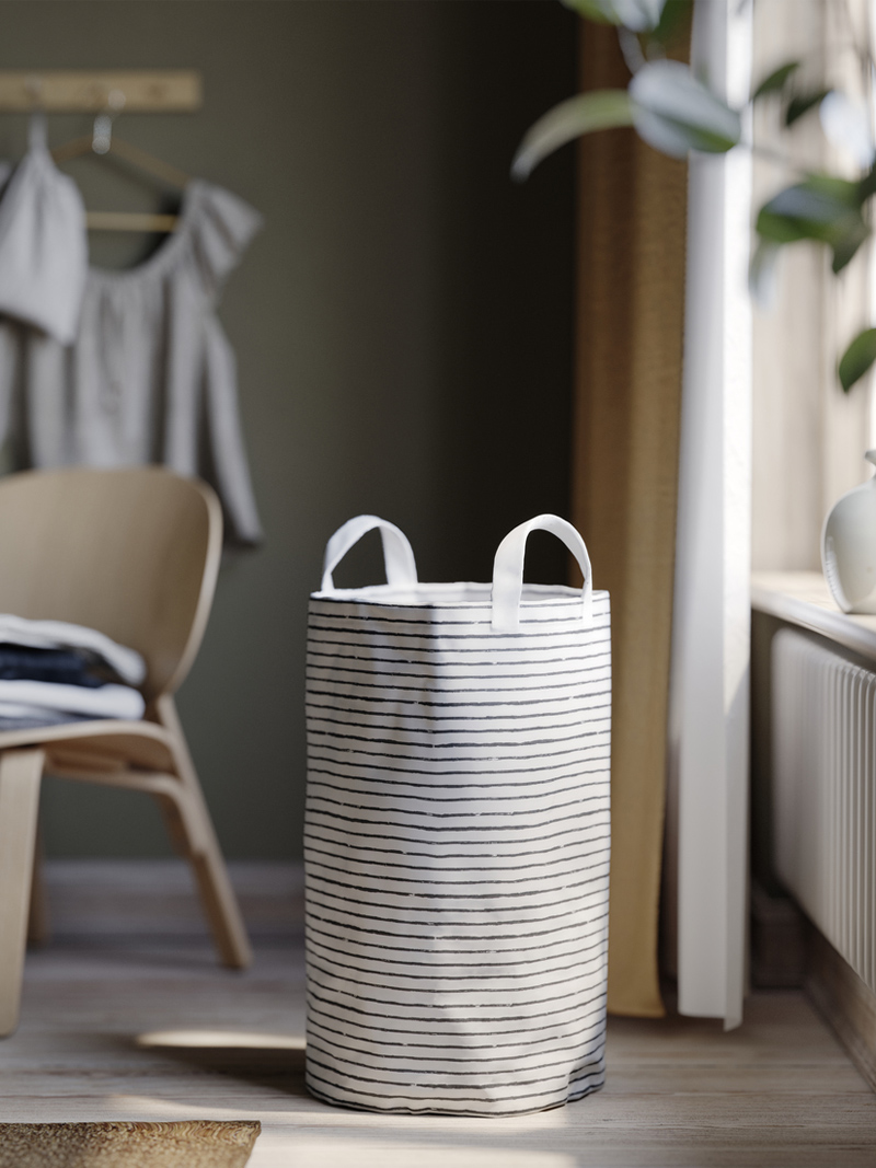 Bolsa de lavandería KLUNKA a rayas blancas y negras en rincón luminoso con mobiliario de madera.