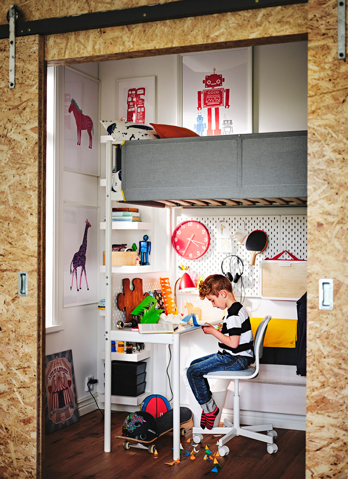 Una habitación infantil con paredes claras, cama alta gris, escritorio blanco con silla y decoraciones coloridas. Ambiente creativo y organizado.