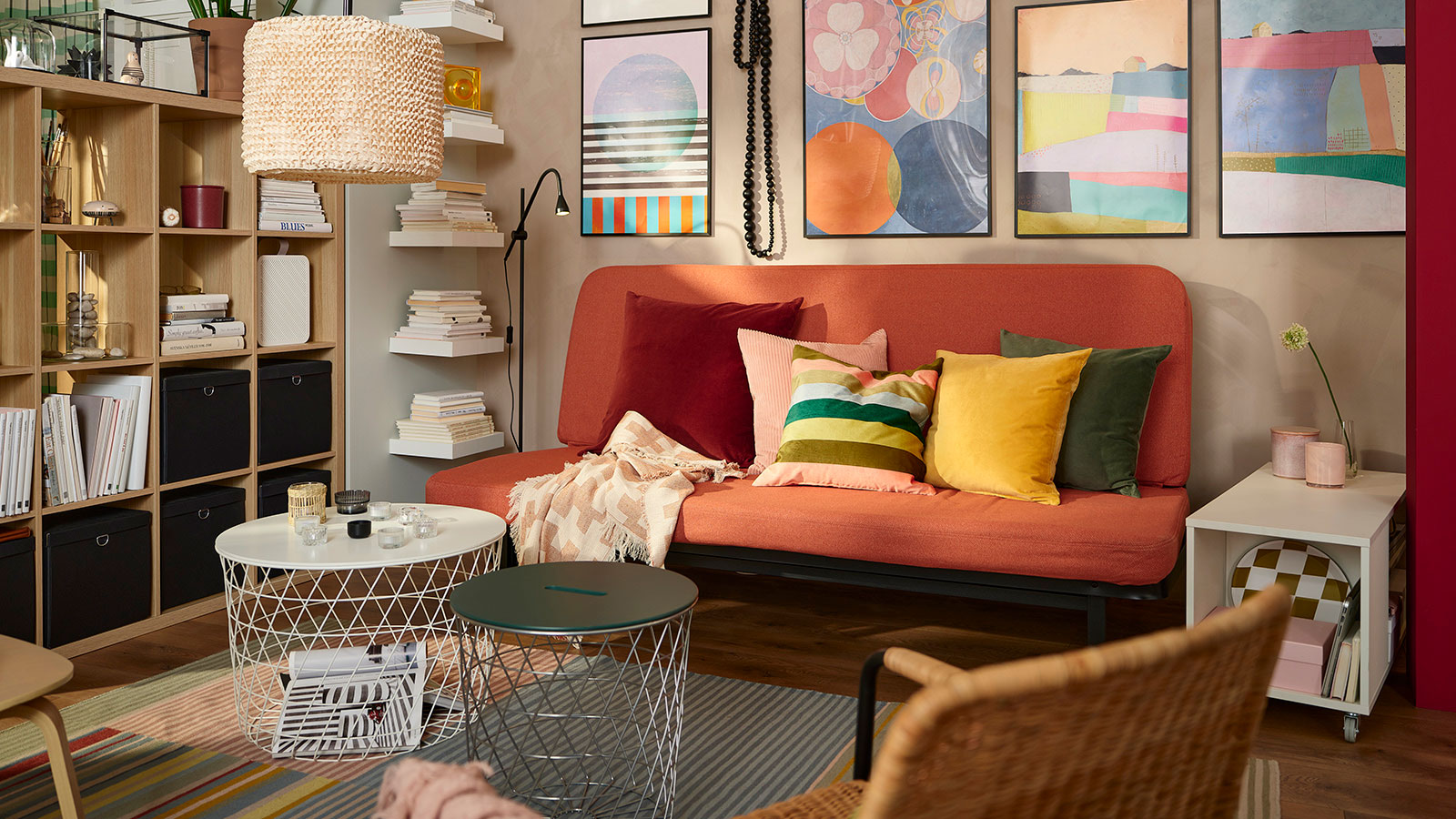 Ambiente colorido con un sofá minimalista con varios cojines multicolores, estilo años 70, hay una estantería abierta de madera de pino,