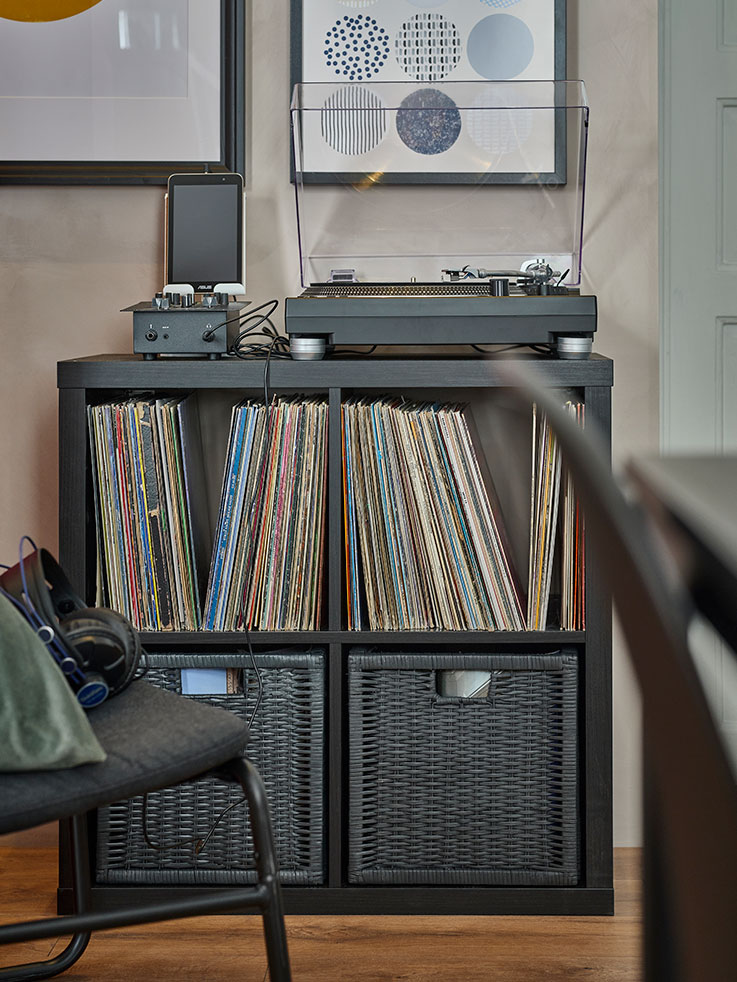 armario abierto con cuatro espacios, con cajas de mimbre en el inferior y lleno de discos de vinilo en la parte superior, hay un tocadiscos en la parte superior
