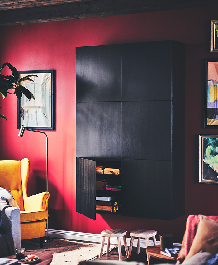 Living room with red wall, black wall-mounted cabinet with open door, yellow armchair, and artistic decor.