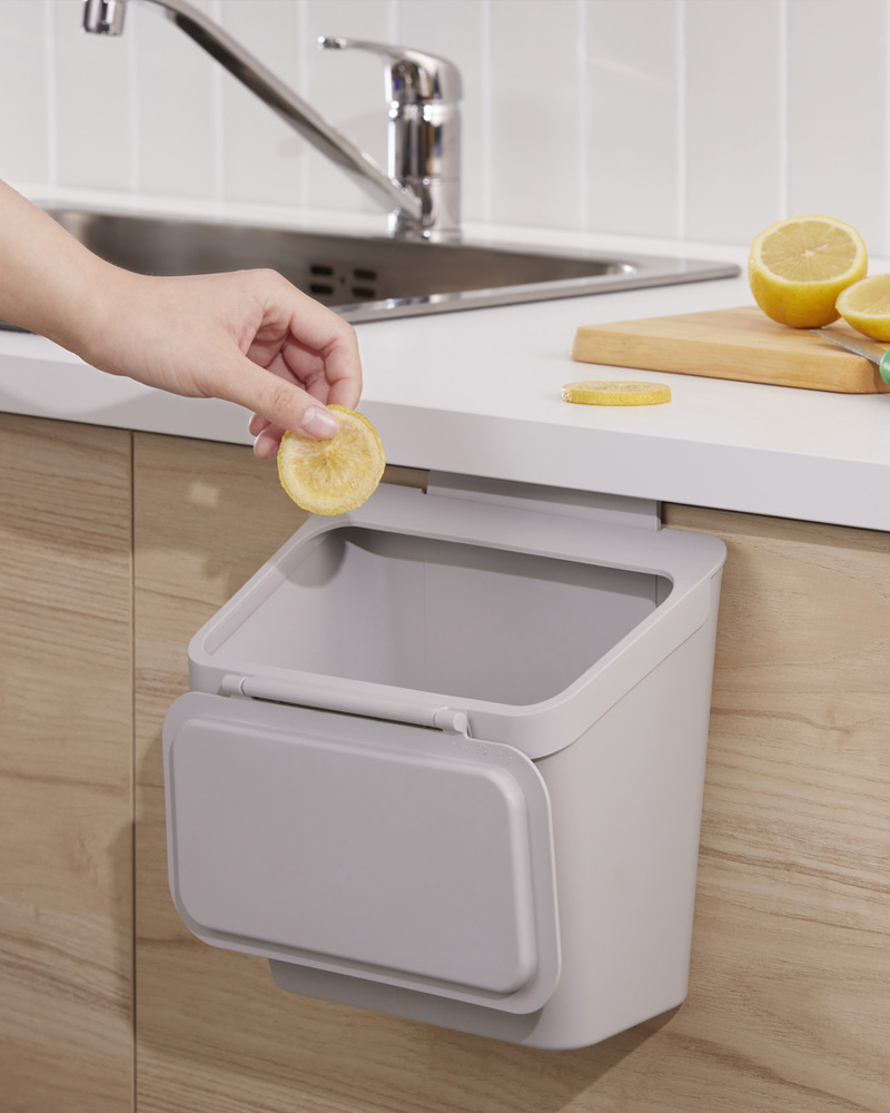 Small trash can hanging on a door near the sink in a white and oak kitchen.