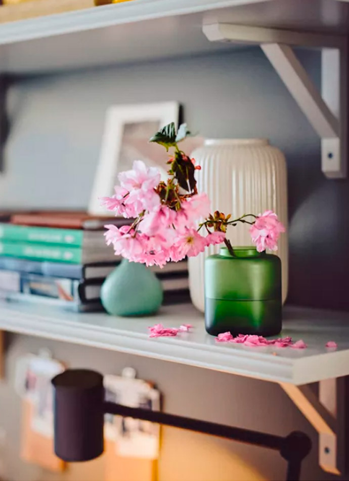 A white shelf displays vases (one with pink blossoms), books, and a picture frame. Homey, bright, and delicate atmosphere.